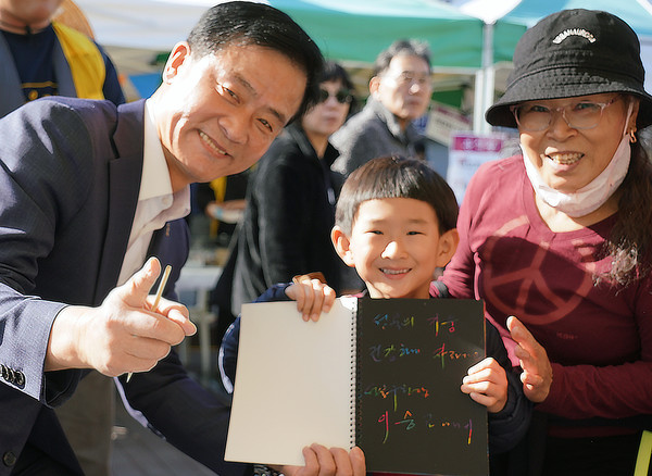 이승로 구청장(맨 왼쪽)이 글씨쓰기 행사 참여후 받은 노트를 아이에게 전달 후 기념촬영을 하고 있다. [성북구 제공]